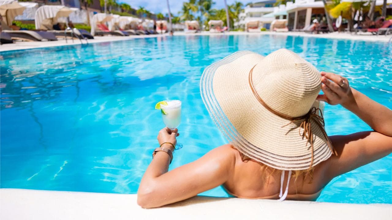 Viajera con sombrero de paja disfrutando de un trago en la piscina de un resort